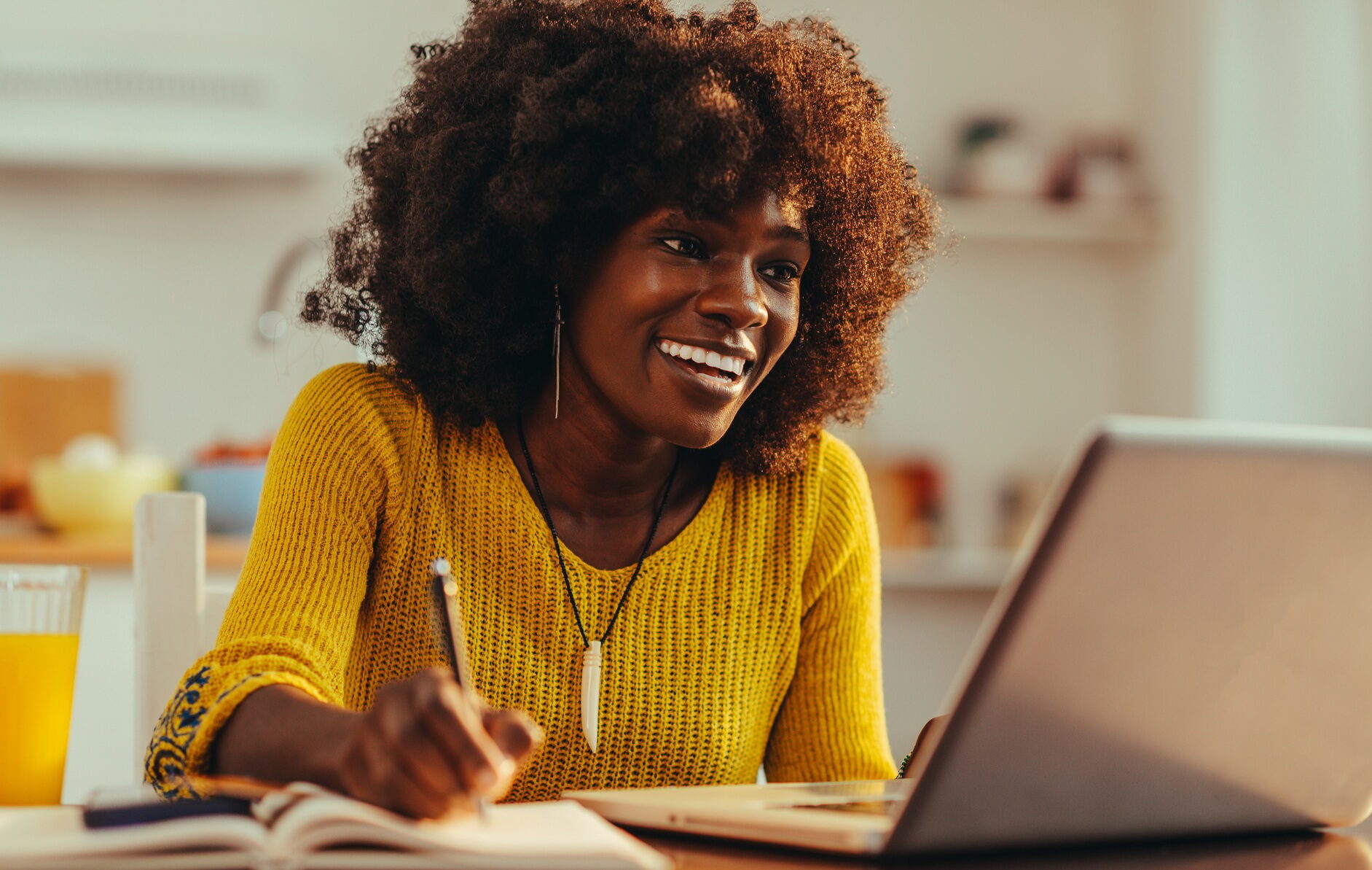 African American woman is smiling at the laptop and writing down in the textbook.