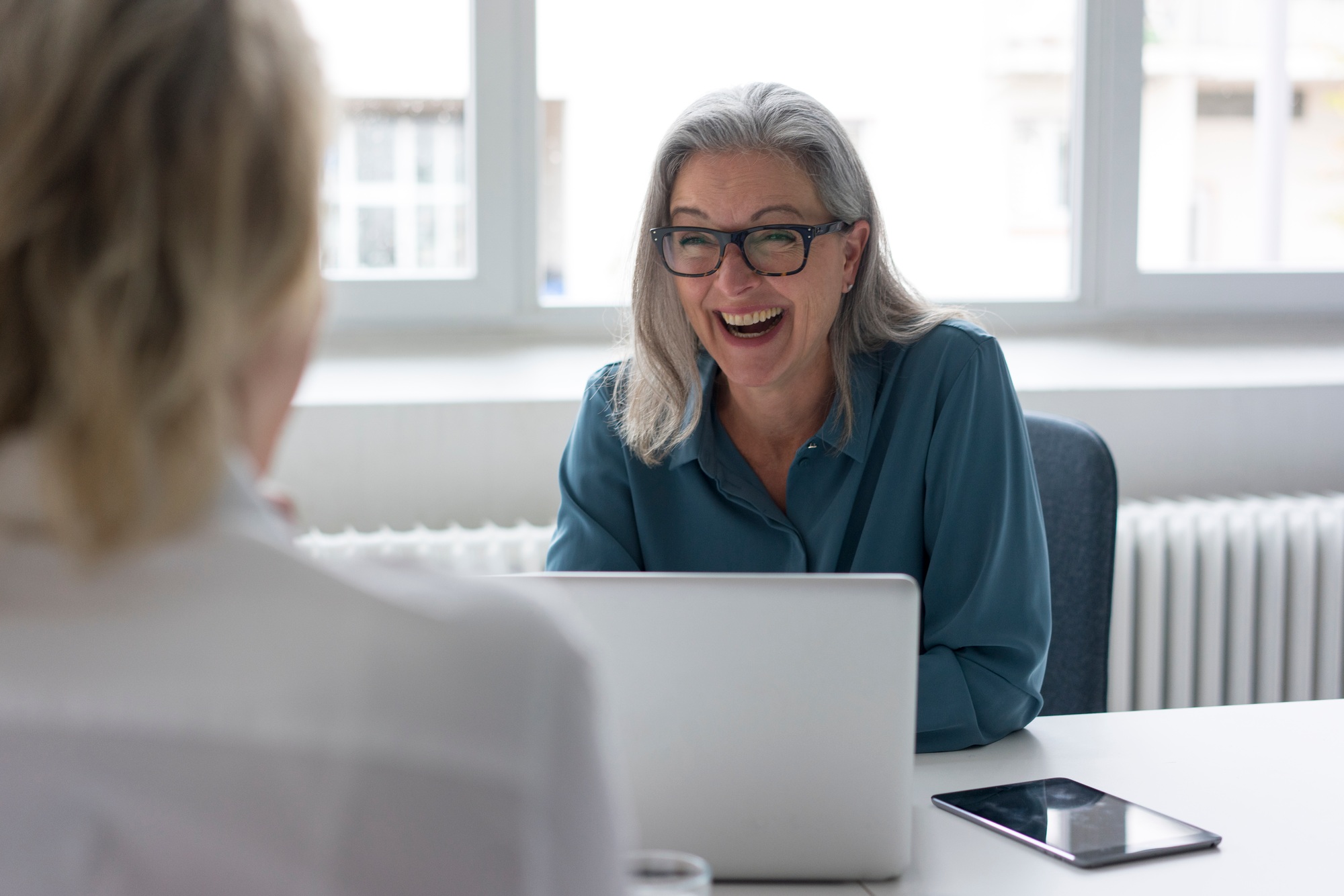 Laughing mature businesswoman talking to young businesswoman at desk in office
